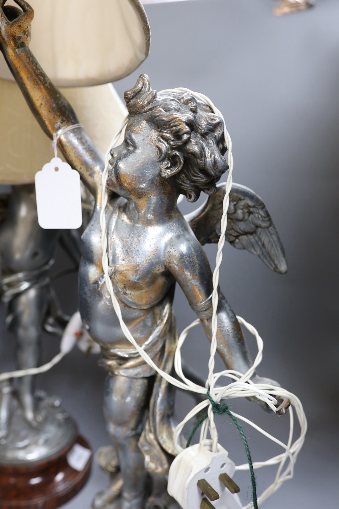 A pair of silvered metal cherub lamps in dancing pose bearing torch lamp, signed L. Gregoire